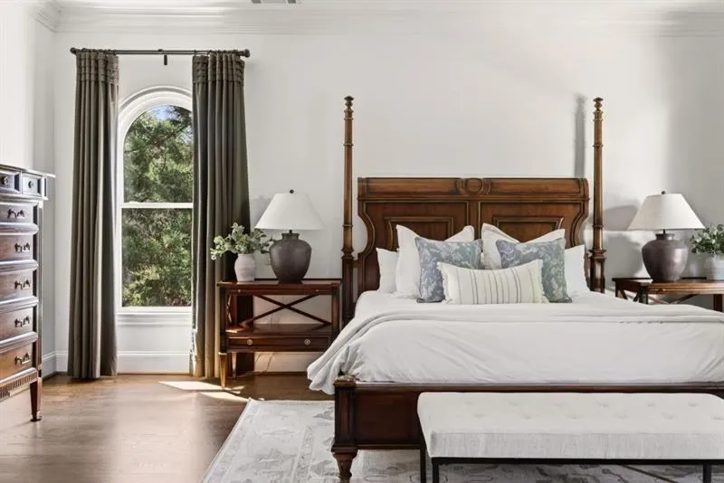 Hardwood-finish flooring featuring an arched window with substantial drapery, crown molding, and a decorative area rug