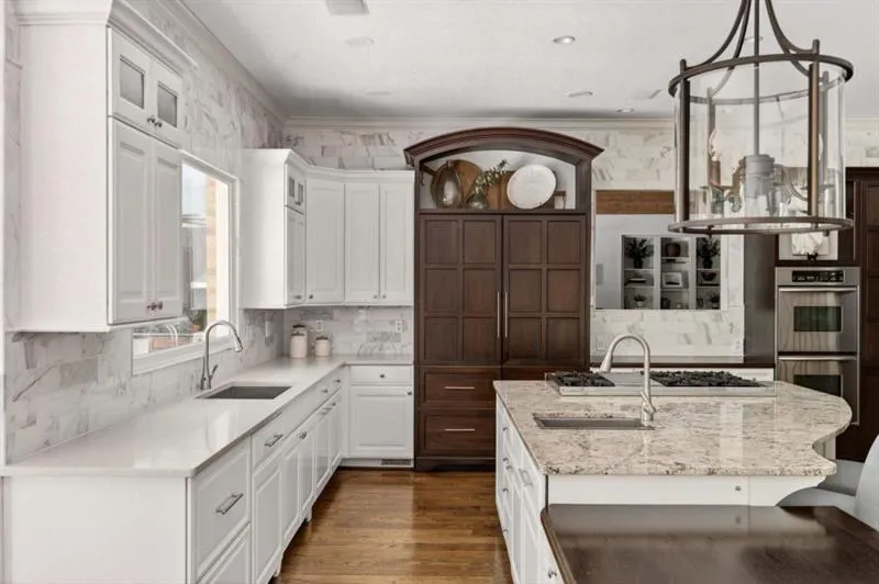 Kitchen featuring white cabinetry, light-toned stone countertops, and a full-height backsplash