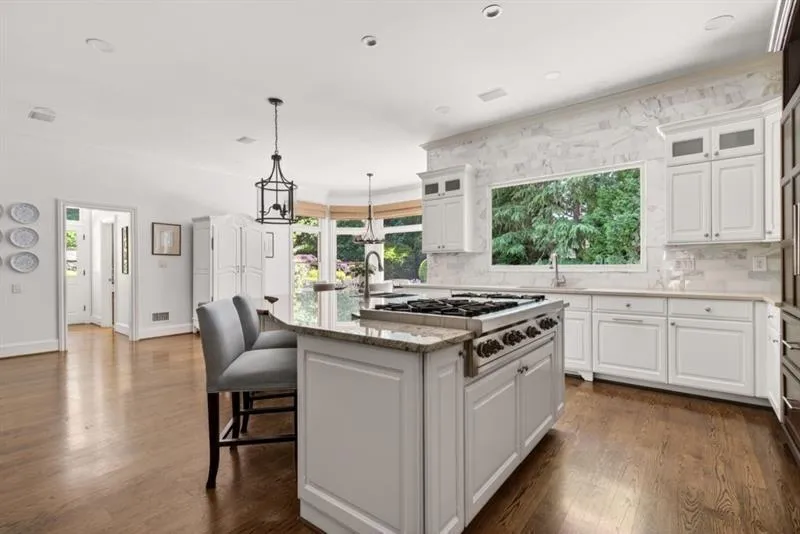 Gourmet kitchen featuring a large island with a gas range, white cabinetry, stone countertops, a full-height stone backsplash, and wood-finish flooring