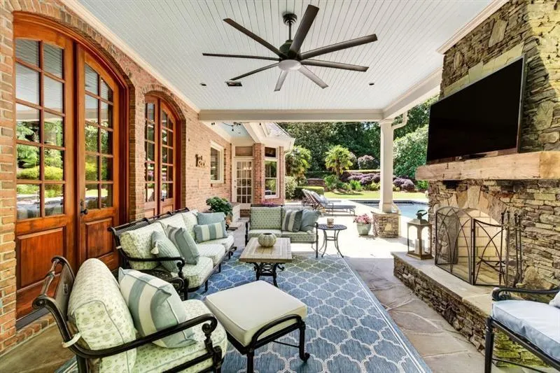 Covered outdoor living area featuring a stone-clad fireplace with a wood mantle, beadboard ceiling, and a ceiling fan