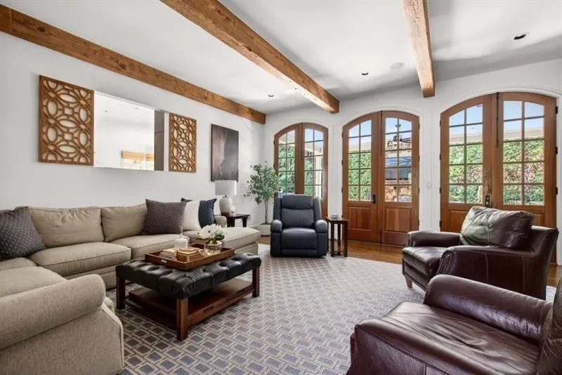 Living area featuring exposed wood ceiling beams, three sets of arched wood-frame French doors, recessed lighting, and wood-finish flooring