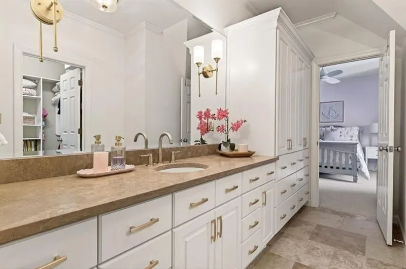 Bathroom vanity featuring dual sinks, a large mirror, extensive built-in cabinetry, and tile flooring