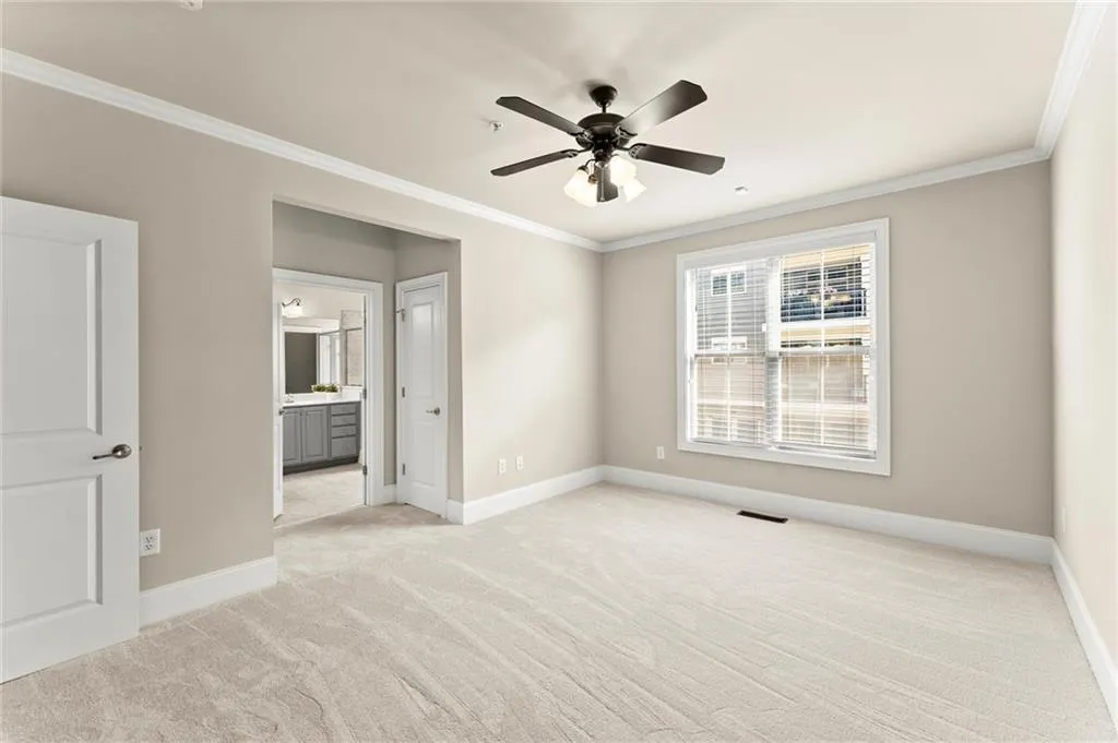 Unfurnished bedroom with ornamental molding, light carpet, a ceiling fan, and connected bathroom