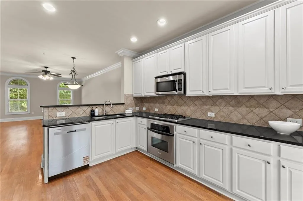 Kitchen featuring white cabinets, ornamental molding, decorative light fixtures, appliances with stainless steel finishes, and backsplash