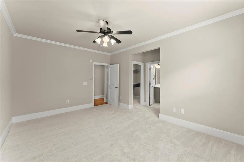Unfurnished bedroom featuring ornamental molding, a walk in closet, light colored carpet, and ceiling fan