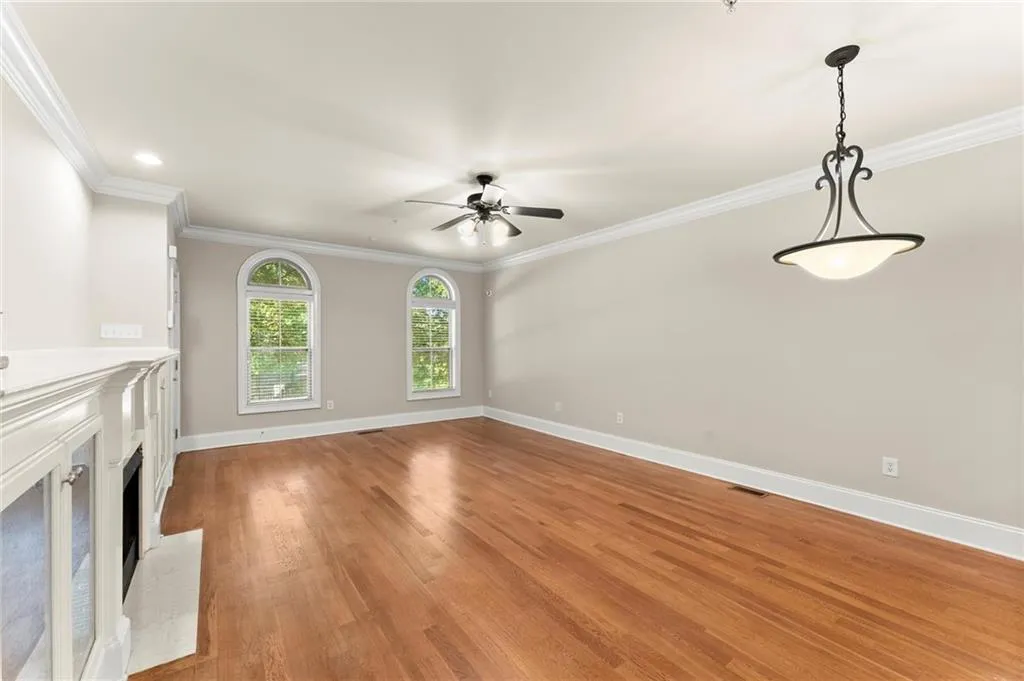 Unfurnished living room with a fireplace with raised hearth, ornamental molding, light wood-style floors, and ceiling fan