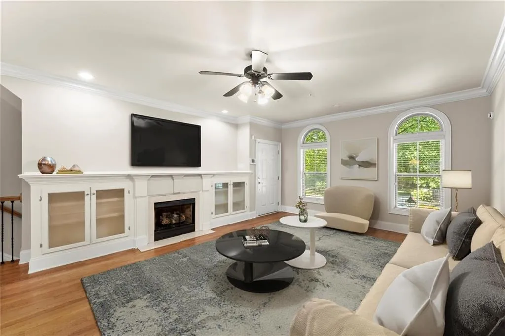 Living area with light wood-style flooring, ornamental molding, a fireplace with flush hearth, and ceiling fan