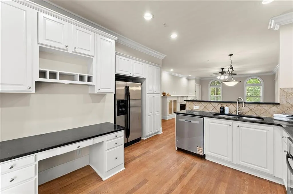 Kitchen with decorative light fixtures, white cabinetry, crown molding, stainless steel appliances, and light wood finished floors