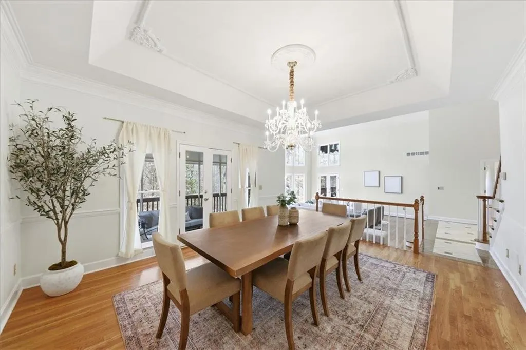 Dining space featuring french doors, a raised ceiling, light wood-style floors, a chandelier, and crown molding