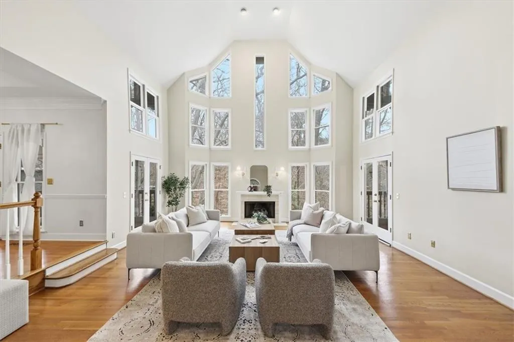 Living room featuring french doors, a fireplace with raised hearth, wood finished floors, and high vaulted ceiling