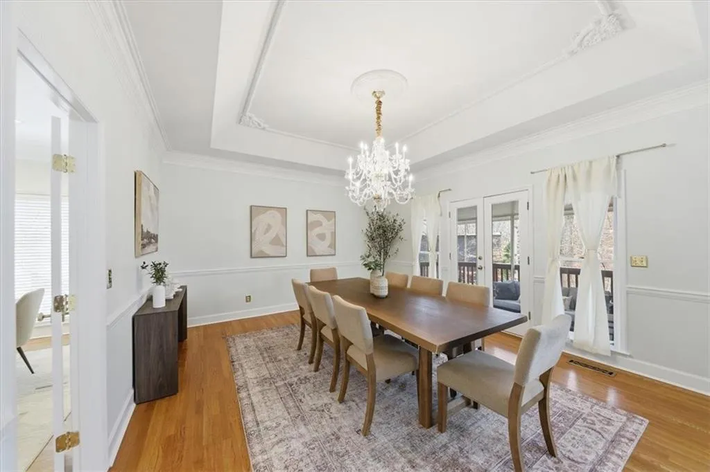 Dining room with french doors, light wood finished floors, a tray ceiling, a chandelier, and ornamental molding