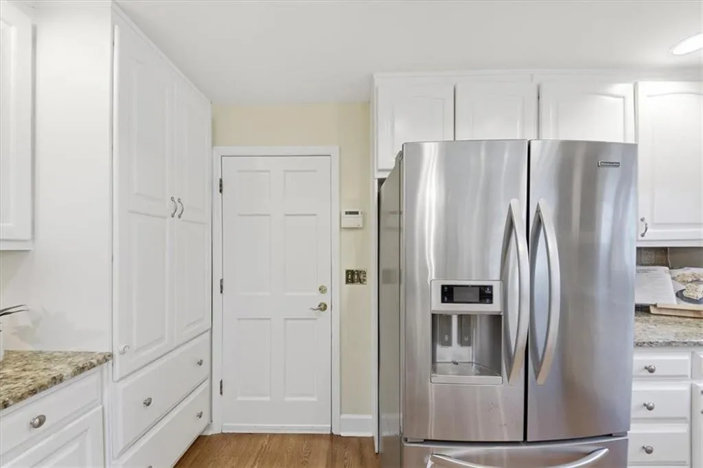 Kitchen featuring white cabinetry, stainless steel fridge with ice dispenser, light stone counters, and light wood-style floors