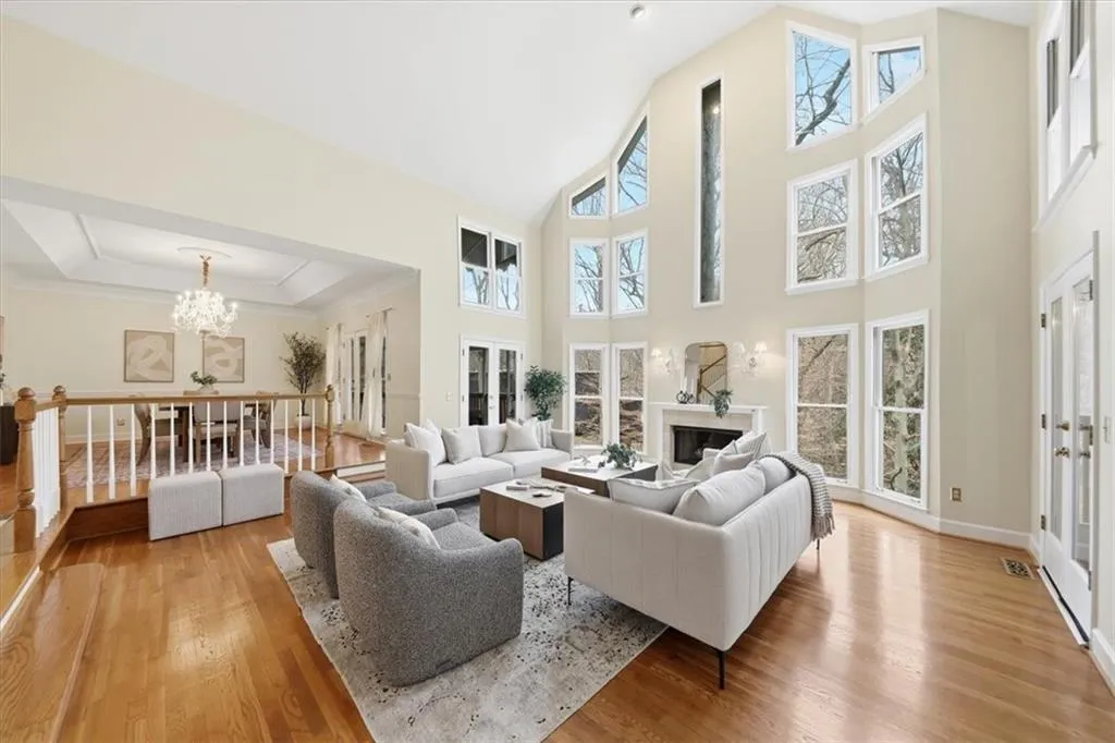 Living room with light wood-type flooring, french doors, a chandelier, a premium fireplace, and high vaulted ceiling