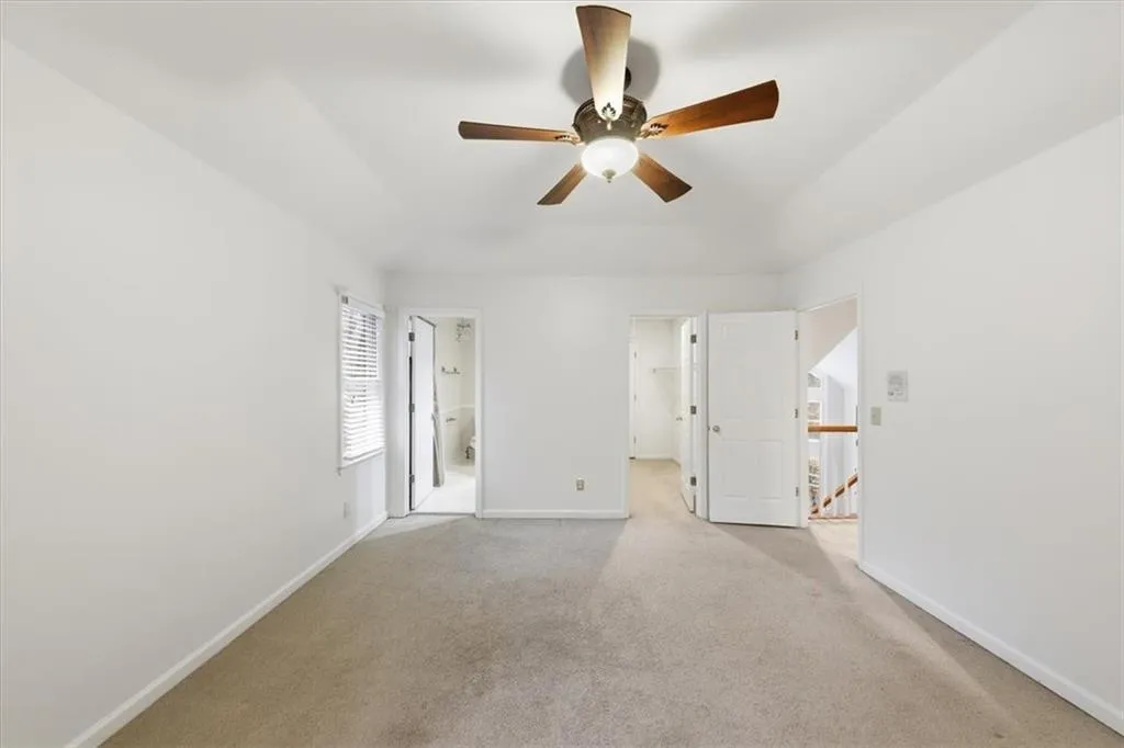 Unfurnished bedroom with a walk in closet, light colored carpet, ceiling fan, and ensuite bath