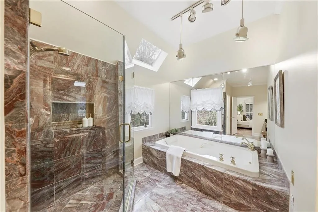 Bathroom with a skylight, a garden tub, a marble finish shower, marble look tile flooring, and track lighting