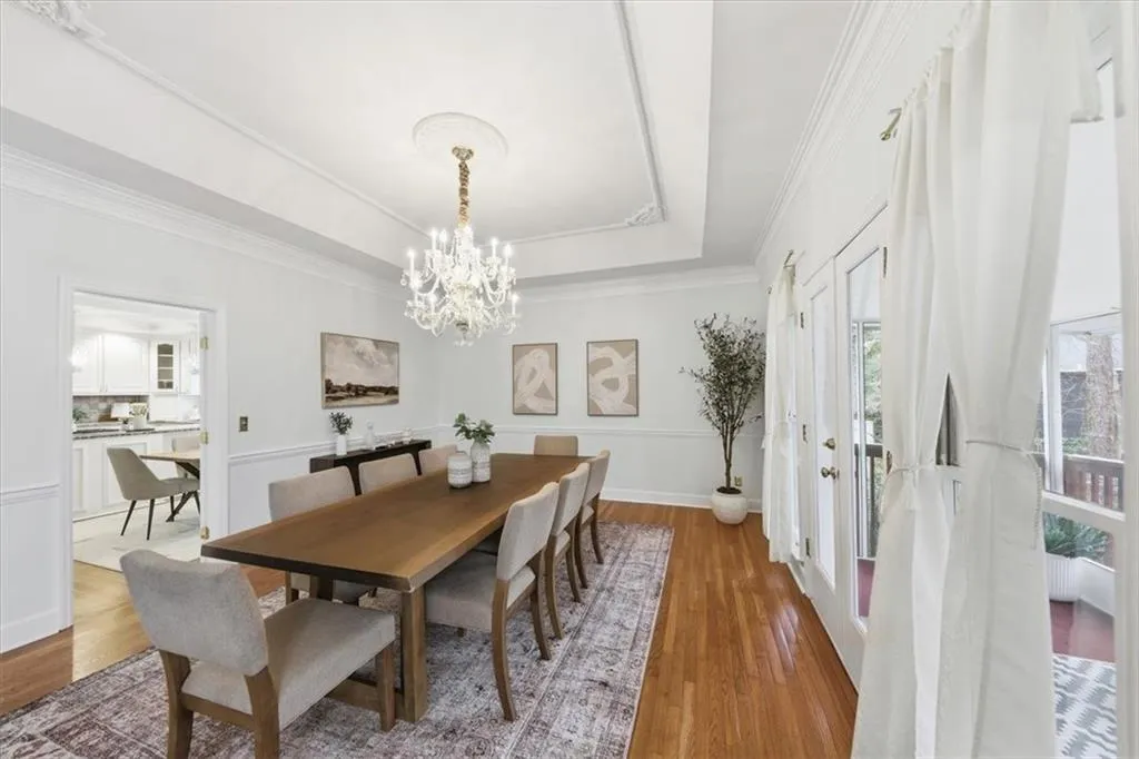 Dining area with wood finished floors, a chandelier, a tray ceiling, and ornamental molding