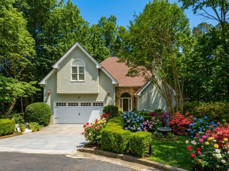 Stucco exterior with a peaked roofline, arched window, and attached two-car garage