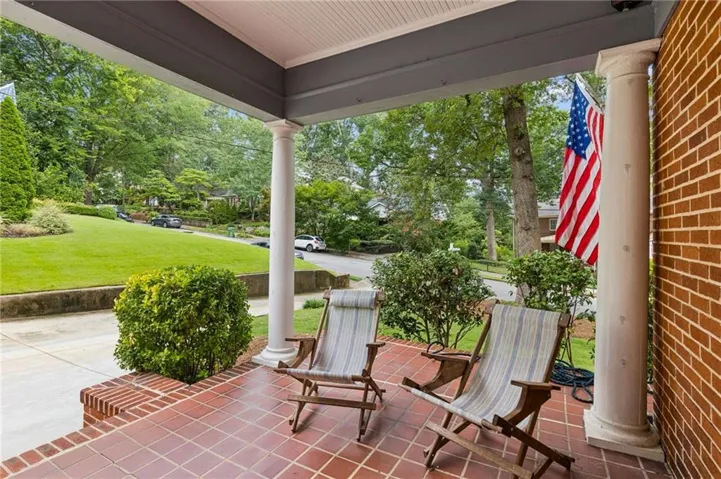 Inviting covered porch with a terra cotta tile floor, brick knee wall, and classical columns