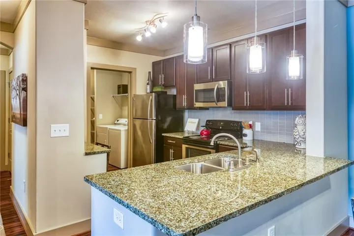 Kitchen featuring hardwood / wood-style floors, washer and dryer, kitchen peninsula, hanging light fixtures, and appliances with stainless steel finishes