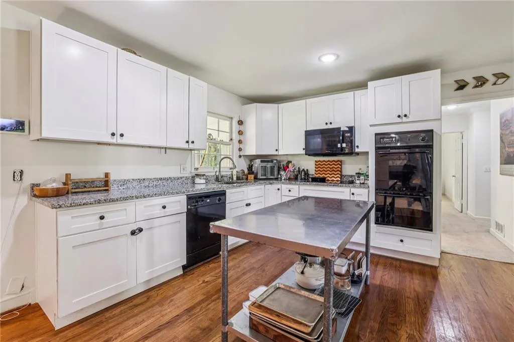 Kitchen featuring white cabinets, light stone countertops, dark wood-type flooring, black appliances, and recessed lighting