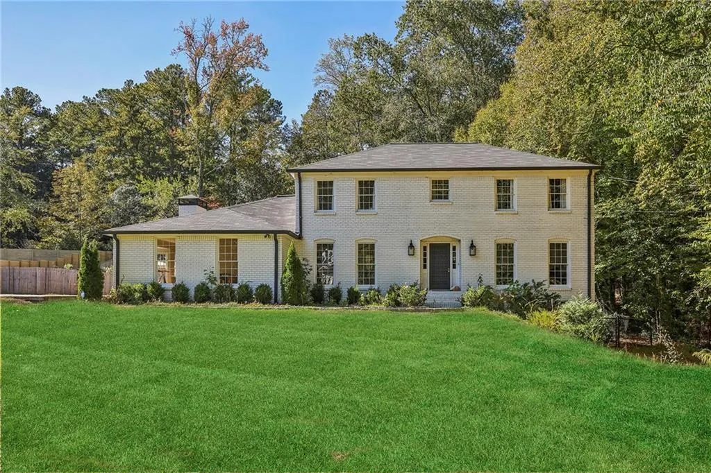 Colonial house with brick siding, a chimney, and view of scattered trees
