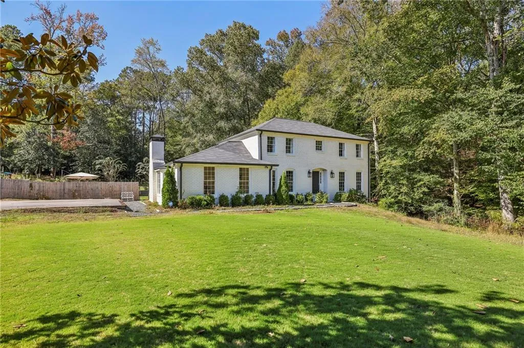 Colonial-style house featuring a chimney, view of wooded area, and brick siding