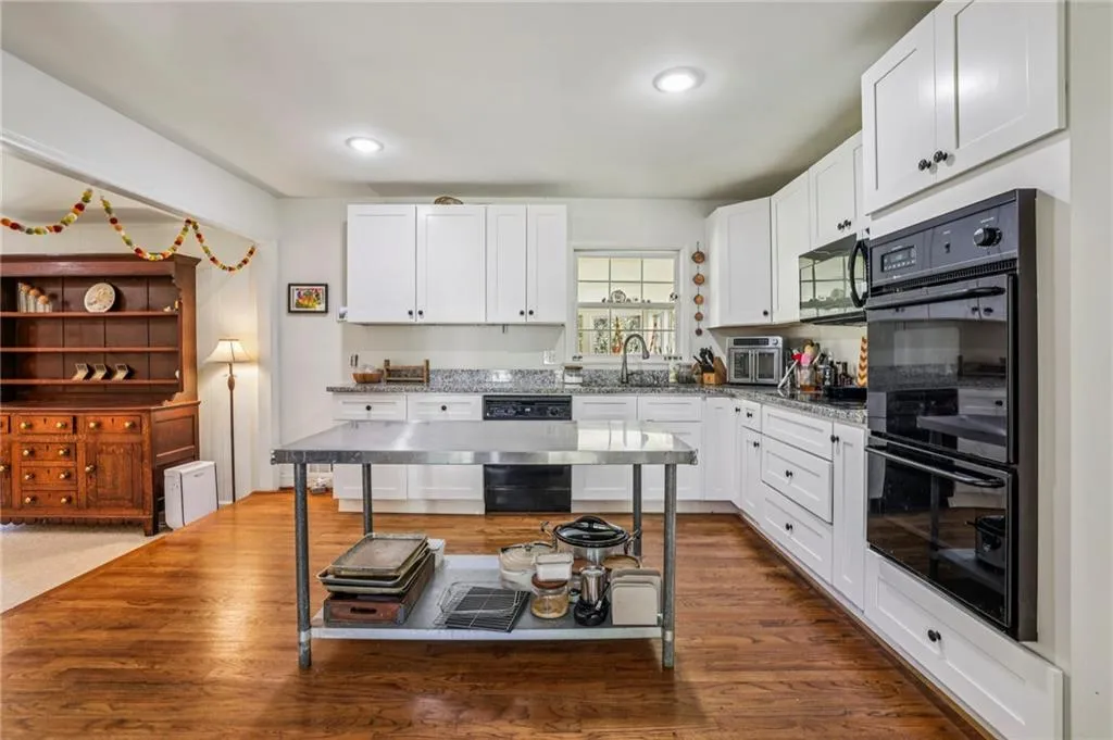 Kitchen with black appliances, white cabinets, light stone counters, dark wood-style floors, and recessed lighting