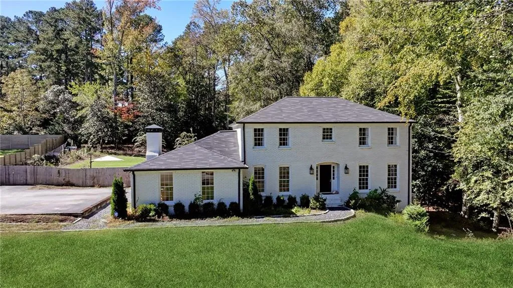 Colonial inspired home with brick siding, a chimney, and view of scattered trees