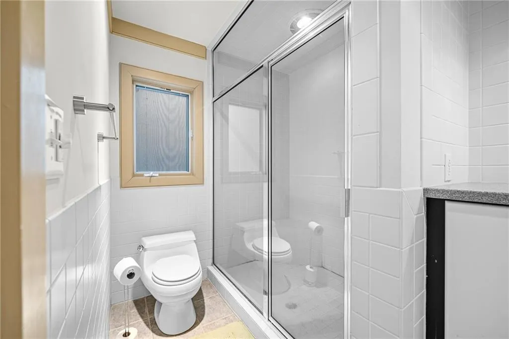 Bathroom with tile walls, vanity, a shower stall, and light tile patterned flooring