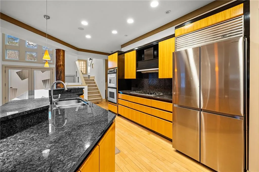 Kitchen with stainless steel appliances, hanging light fixtures, dark stone countertops, light wood-type flooring, and recessed lighting