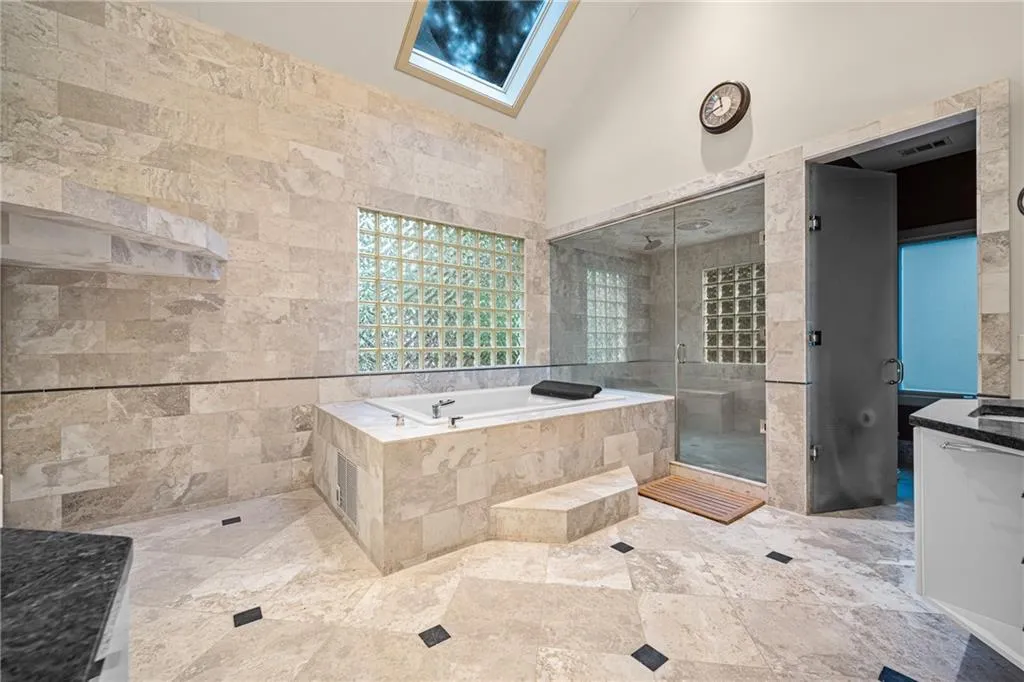 Full bathroom with a stall shower, a garden tub, tile walls, vanity, and vaulted ceiling