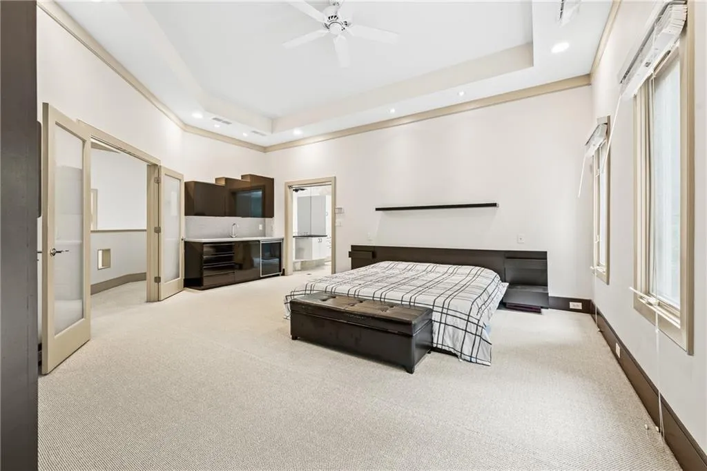 Bedroom featuring light colored carpet, a raised ceiling, ceiling fan, recessed lighting, and beverage cooler