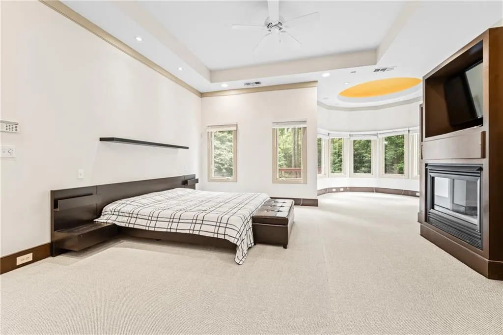Carpeted bedroom with a raised ceiling, a multi sided fireplace, recessed lighting, and a ceiling fan