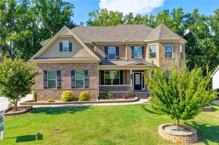 Two-story residence featuring a stone and brick exterior, a covered front porch with white railing, and a prominent turret architectural detail
