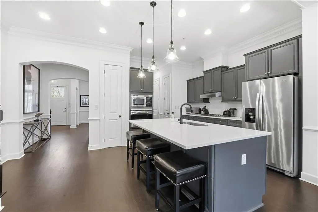 Kitchen featuring arched walkways, appliances with stainless steel finishes, decorative light fixtures, ornamental molding, and a kitchen breakfast bar