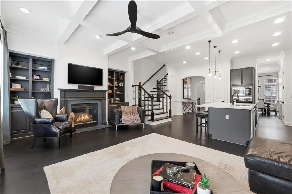 Living room with coffered ceiling, built in features, stairway, beamed ceiling, and a fireplace with flush hearth