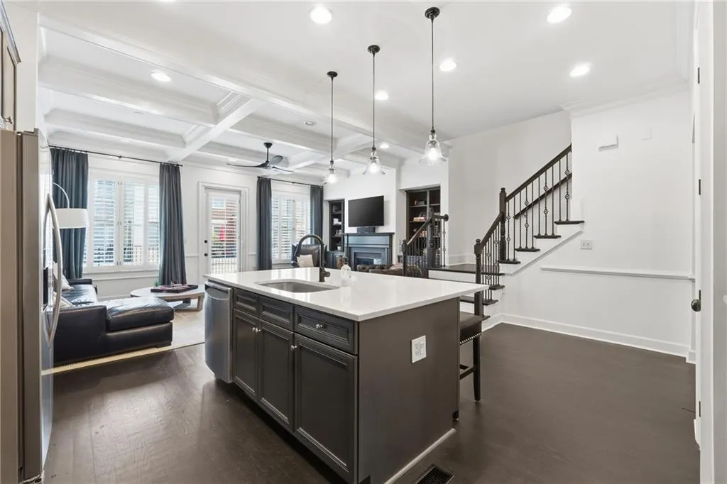 Kitchen with open floor plan, beam ceiling, coffered ceiling, decorative light fixtures, and an island with sink