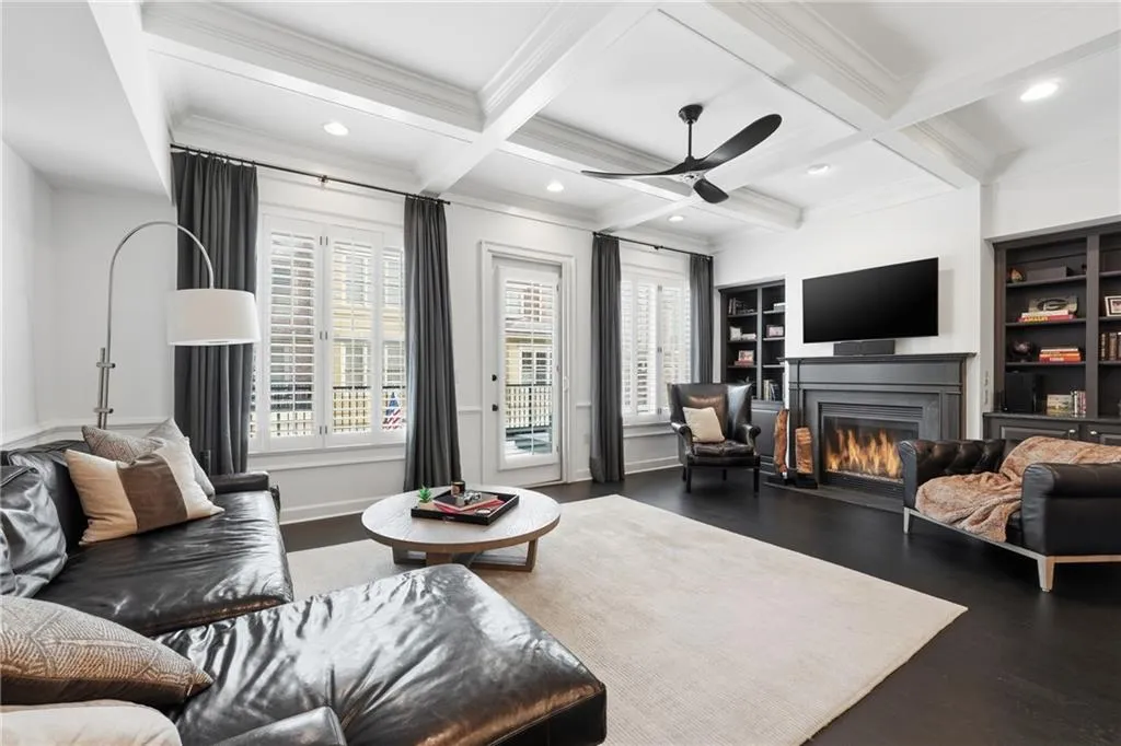 Living area with a glass covered fireplace, coffered ceiling, built in shelves, beamed ceiling, and wood finished floors