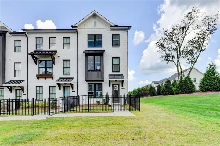 White brick exterior with black framed windows, a gabled roofline, and a black metal fence