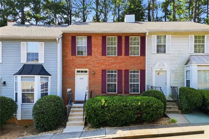 Red brick exterior featuring white paneled entry door with black hardware, burgundy window shutters, and mature front landscaping