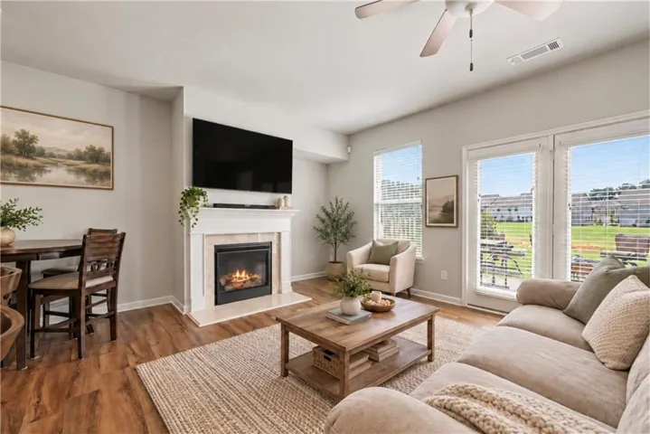 Living area featuring wood-finish flooring, a fireplace with a light-colored mantel, a ceiling fan, and multiple windows