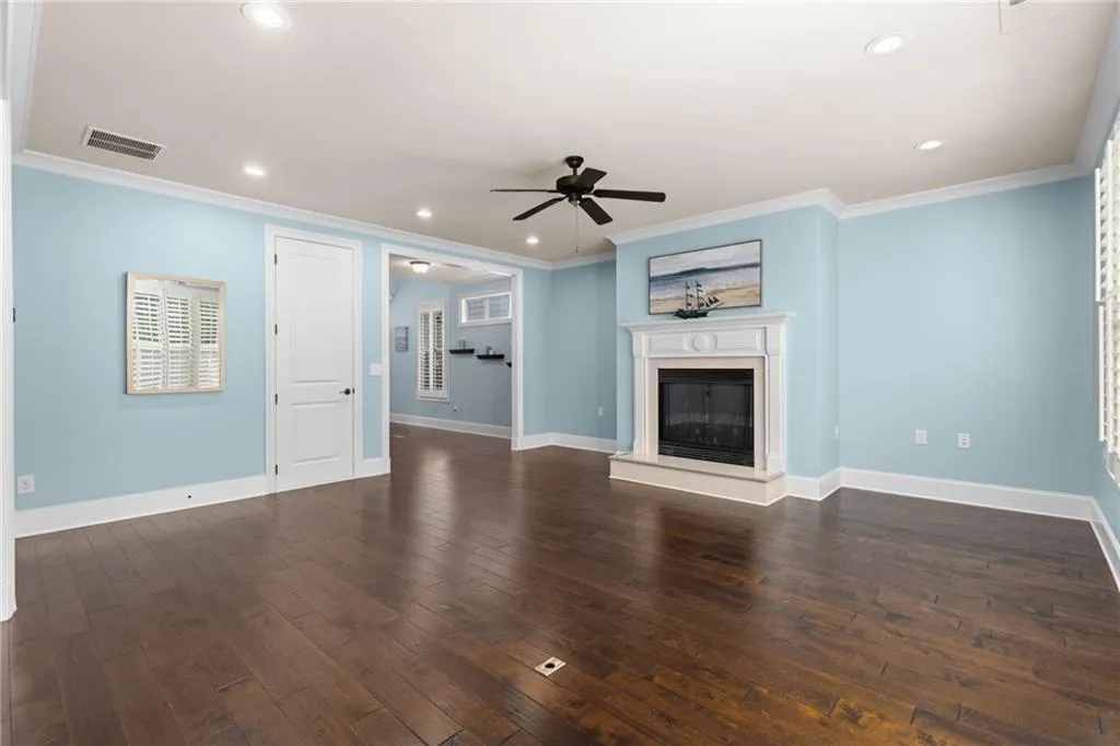 Unfurnished living room featuring dark hardwood / wood-style floors, ceiling fan, and crown molding