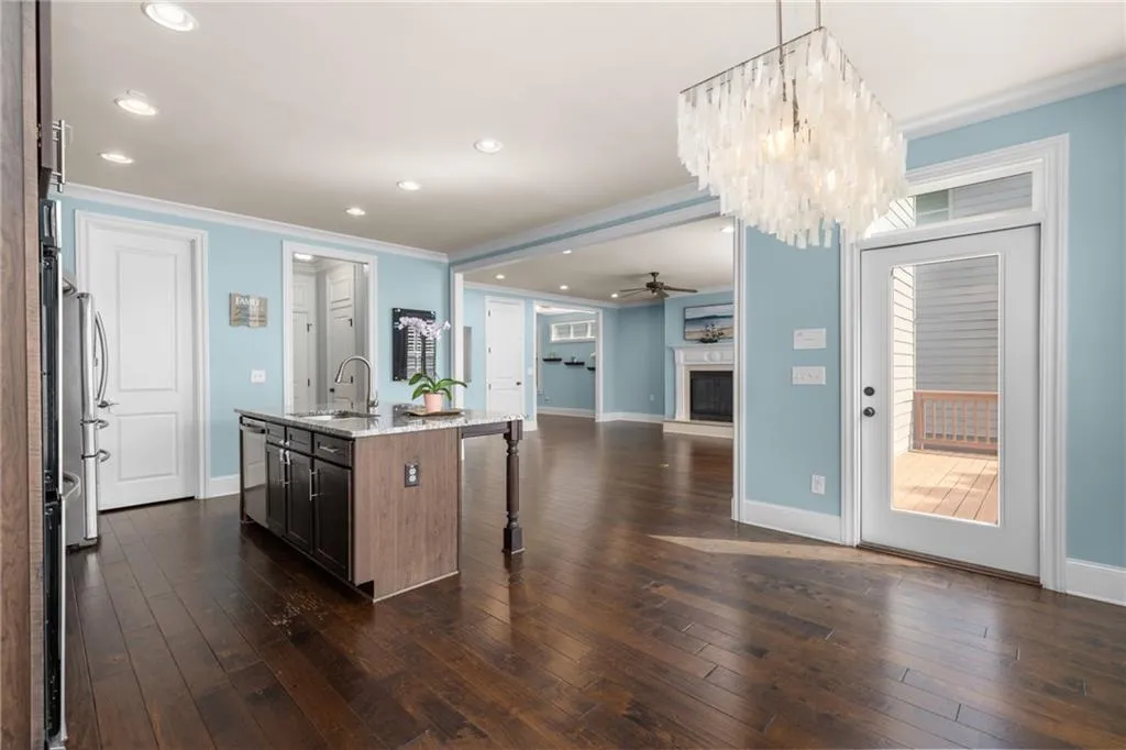 Kitchen featuring a center island with sink, ceiling fan with notable chandelier, dark hardwood / wood-style flooring, light stone counters, and sink