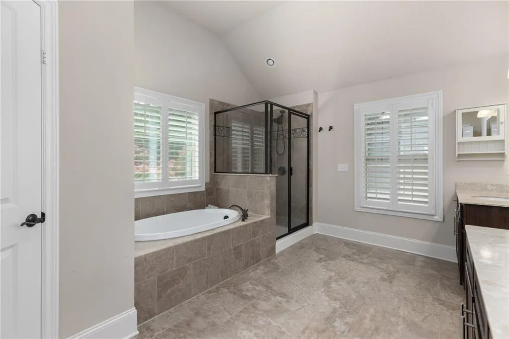 Bathroom with lofted ceiling, vanity, tile floors, and plus walk in shower