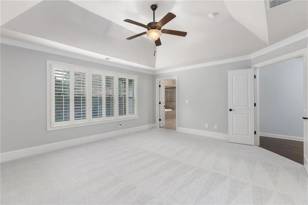 Unfurnished bedroom with ceiling fan, carpet floors, and ensuite bathroom