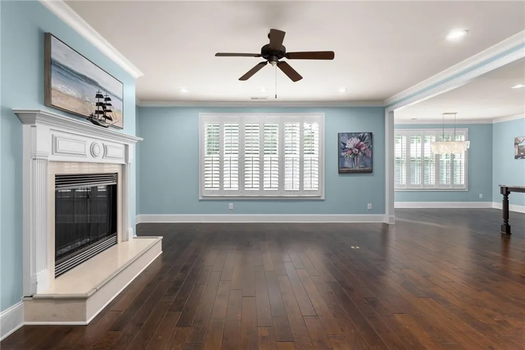 Unfurnished living room featuring dark hardwood / wood-style flooring, ornamental molding, and ceiling fan with notable chandelier