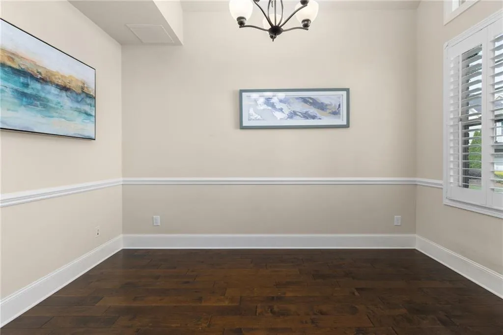 Unfurnished room with dark wood-type flooring and an inviting chandelier