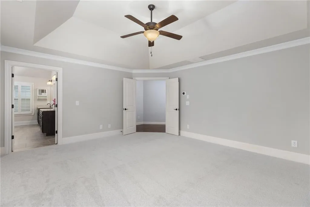 Unfurnished bedroom featuring crown molding, a tray ceiling, connected bathroom, carpet floors, and ceiling fan