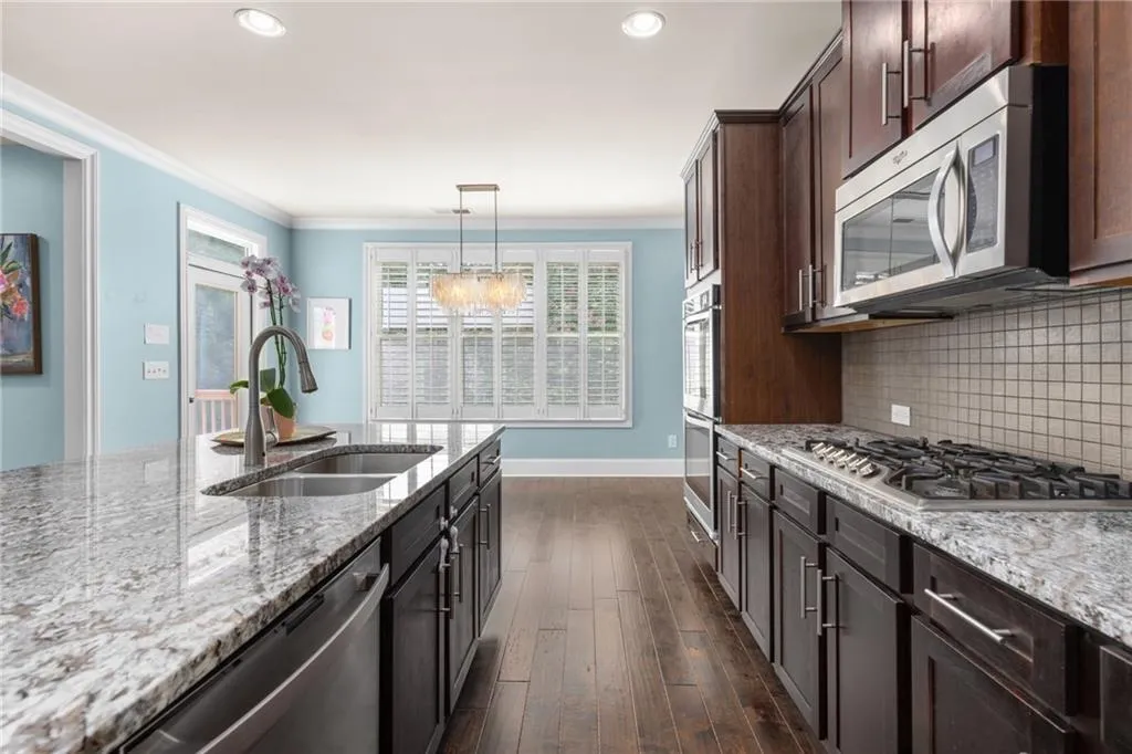 Kitchen featuring tasteful backsplash, dark wood-type flooring, hanging light fixtures, sink, and appliances with stainless steel finishes