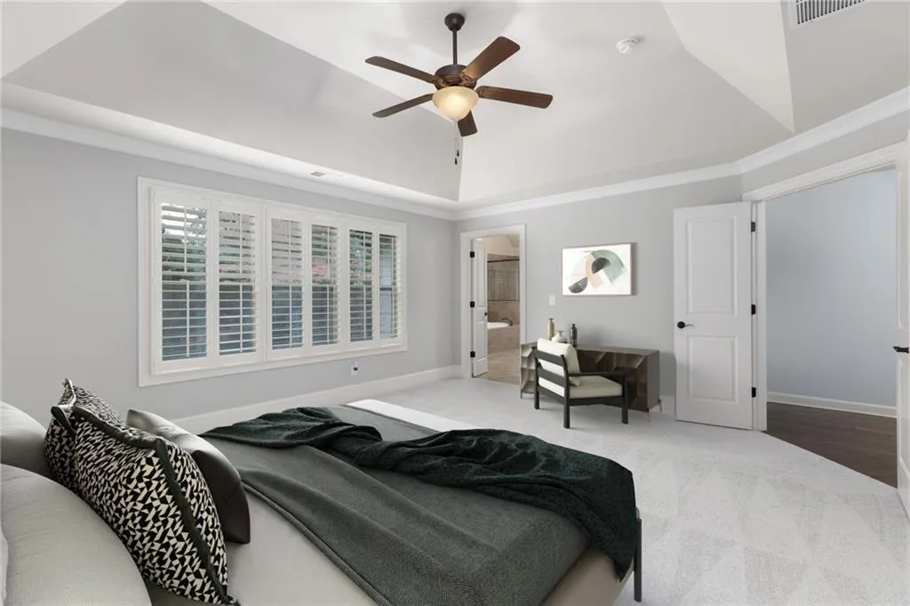 Carpeted bedroom with vaulted ceiling, connected bathroom, ceiling fan, and a raised ceiling